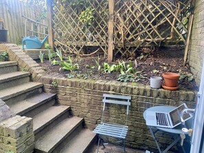 Un jardin avec des marches menant à un mur de briques, une chaise en métal, une table avec un ordinateur portable et une clôture en bois.