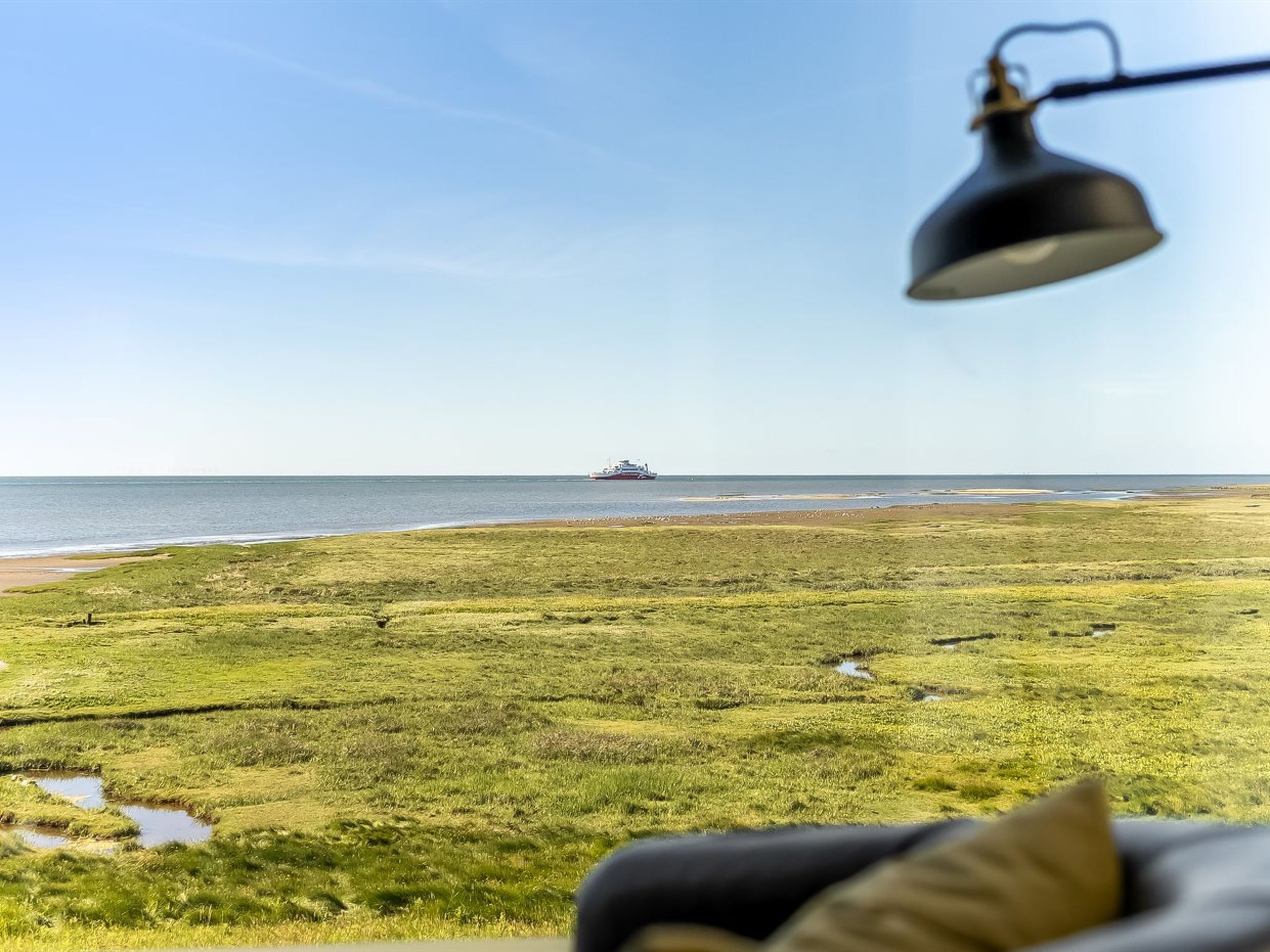 Uitzicht op een grasveld met een schip in de verte, een lamp en een onscherp object op de voorgrond.