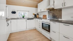 Eine moderne Küche mit weißen Schränken, einer Holzbalkendecke und einem Fenster mit Blick auf Bäume.