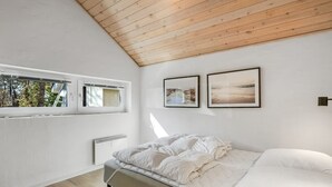 Ein modernes Schlafzimmer mit schrägem Dach, einem Bett, einem Fenster und zwei gerahmten Bildern an der Wand.
