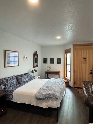 A bedroom with a large bed, a wooden dresser, a desk with a lamp, and a wardrobe. - Speak Easy Eugene, Oregon. Located between Downtown and Whiteaker District (Eugene)