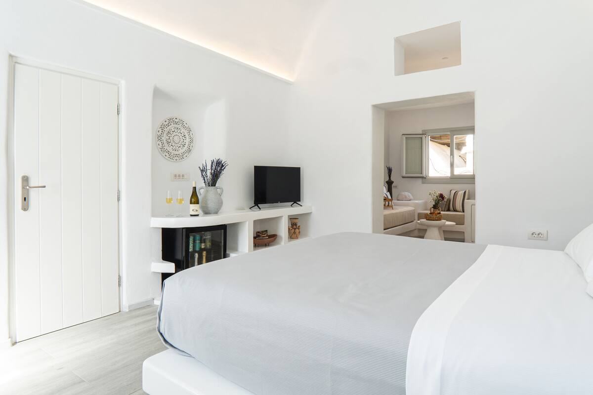 A modern bedroom with a large bed, a TV, a vanity with a mirror, and a door.
