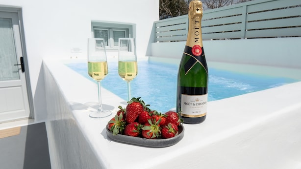 A bottle of Moët & Chandon champagne, two glasses of white wine, and a bowl of strawberries on a white balcony with a pool in the background. - Santorinico villas  (Imerovigli)