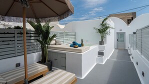 A modern outdoor seating area with a bench, a small table, and a potted plant. - Santorinico villas  (Imerovigli)