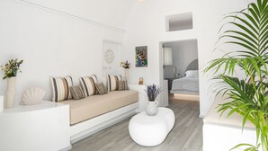 A modern living room with a sofa, a round coffee table, and a potted plant. - Santorinico villas  (Imerovigli)