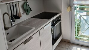 A kitchen with a sink, stove, and oven, wooden cabinets, and a window with blinds. - Charming T2 near Avignon festival (Montfavet)