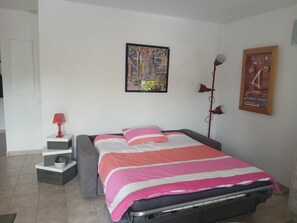A bedroom with a bed, a wall-mounted lamp, a poster, and a small plant. - Charming T2 near Avignon festival (Montfavet)
