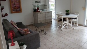 A modern living room with a grey sofa, a small table, and a dining area with a white table and chairs. - Charming T2 near Avignon festival (Montfavet)