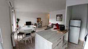 A modern kitchen with a dining area, white cabinetry, a refrigerator, and a flat-screen TV. - Charming T2 near Avignon festival (Montfavet)