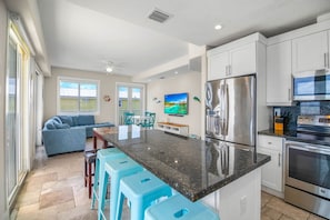 A modern kitchen with a central island, bar stools, stainless steel appliances, and a dining area with a sofa and chairs. - Ocean Views,  Pool, 45’ Dock, Kayaks & 3 Suites (Marathon)
