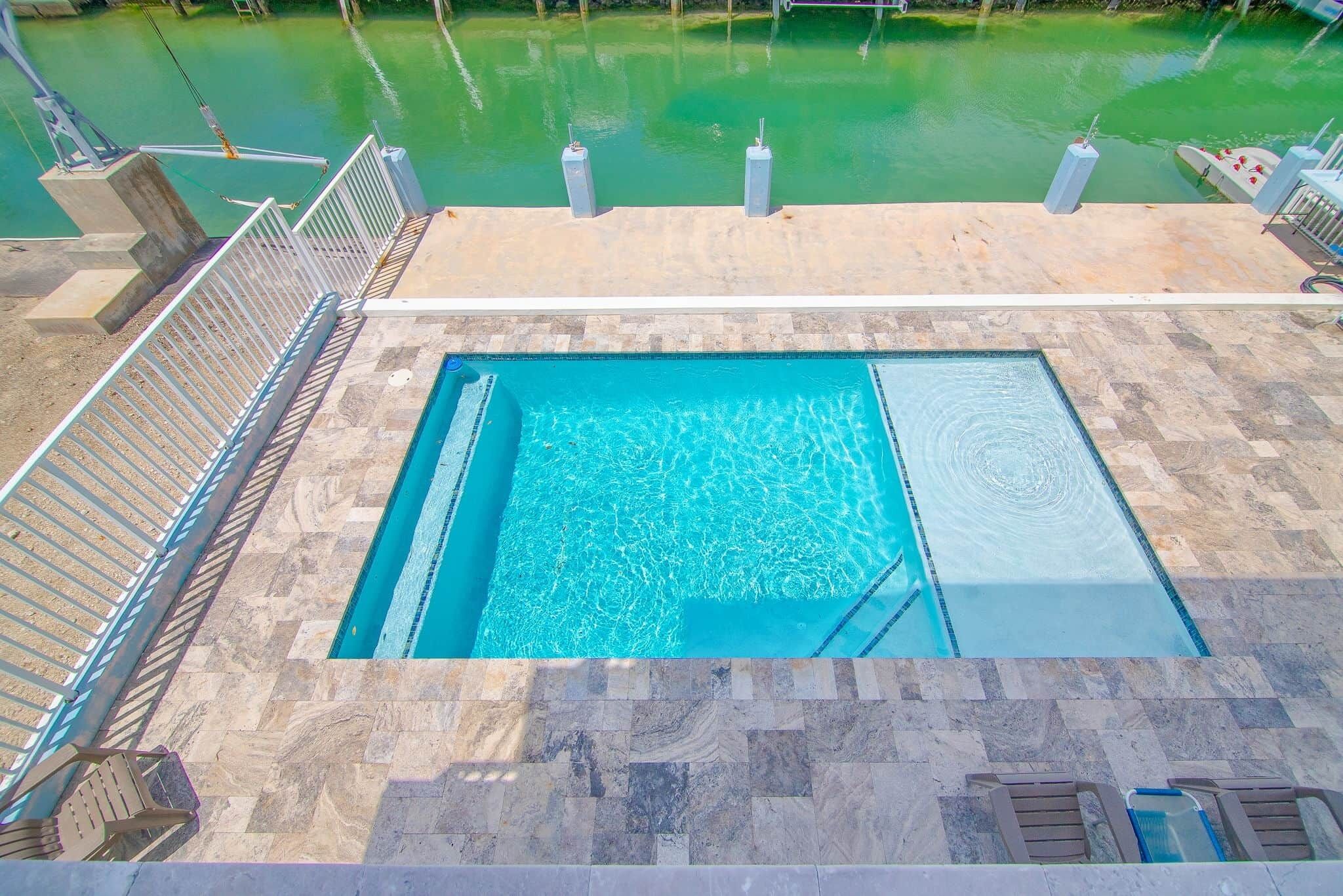 A rectangular pool with clear blue water, surrounded by a stone deck and metal railings.