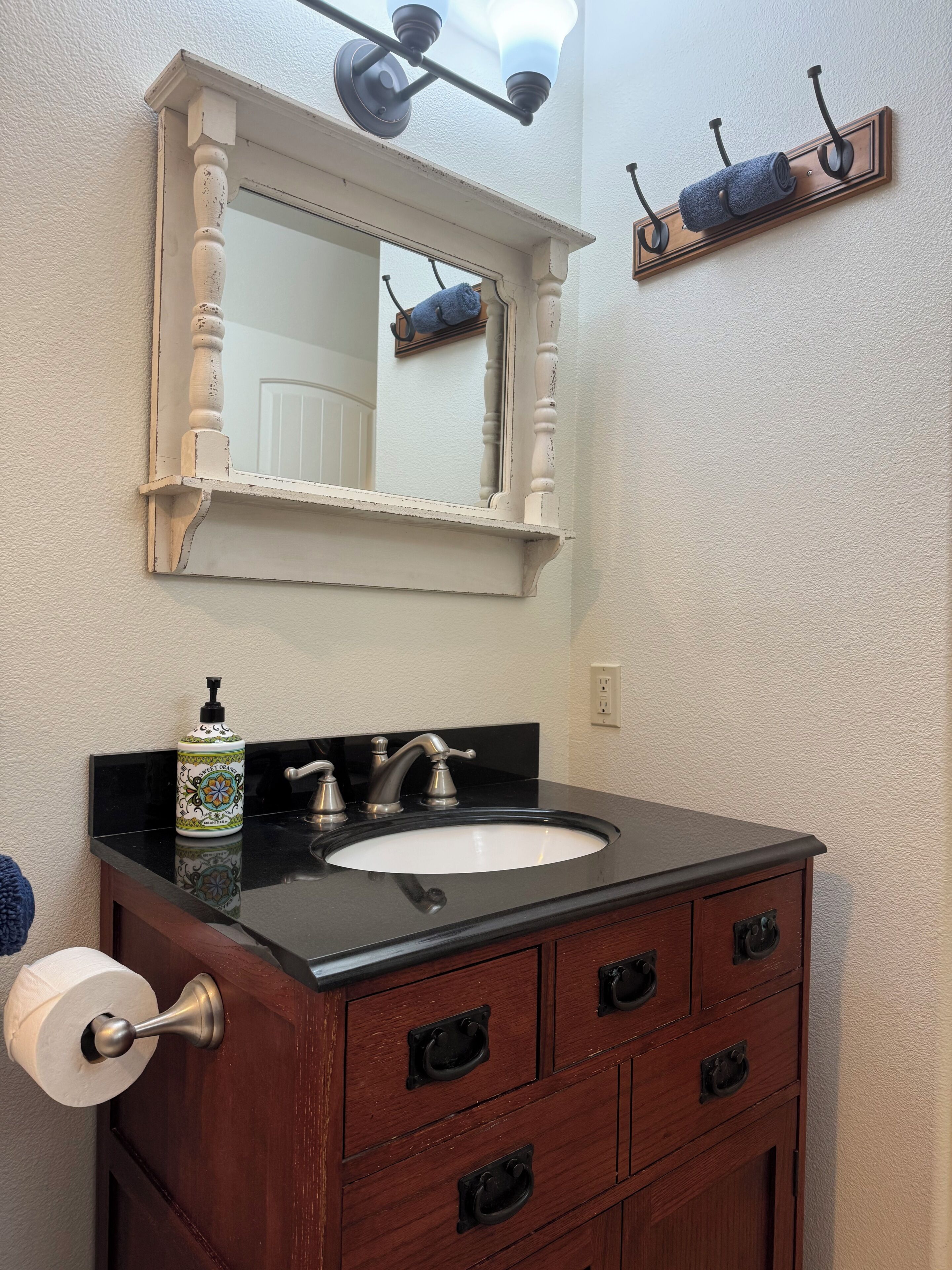 A bathroom with a black sink, wooden vanity, a mirror with a light fixture above, and a towel rack on the wall.