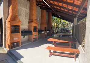 Een terras buiten met barbecuegrills van baksteen, een picknicktafel en een overdekte zithoek.