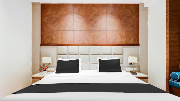 Ein Hotelzimmer mit einem großen Bett, zwei Nachttischen, einem hölzernen Kopfteil und einem Beistelltisch mit einer Lampe.