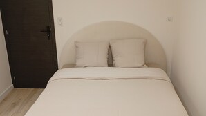A bedroom with a bed, two pillows, a dark door, and a light-colored wall.