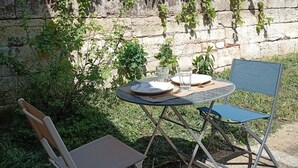 An outdoor dining area with a table and two chairs, surrounded by greenery and a wooden fence.
