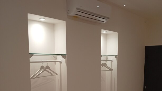 A modern bedroom with a wooden floor, a bed, a wardrobe with a mirror, and an air conditioning unit.
