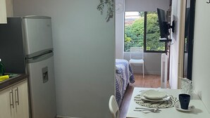 Une cuisine compacte équipée d’un réfrigérateur, d’une table à manger avec des chaises et d’une fenêtre donnant sur un espace verdoyant.