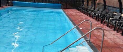 Ein überdachter Swimmingpool mit Glasdecke, Metallleiter und roter Bodenfläche.