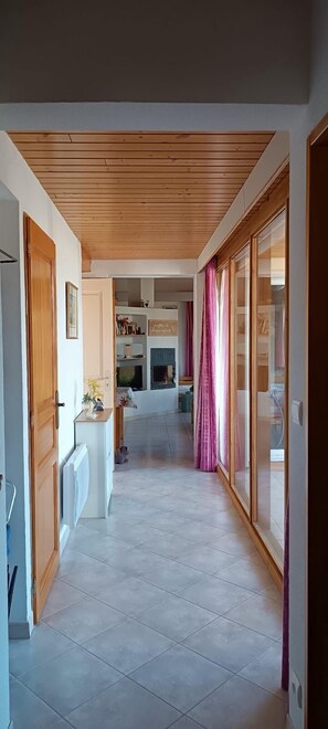 A hallway with a wooden ceiling, a white radiator, a small table with a vase, and a door on the left. - Villa at Domaine de l'Espinet - Quillan 11500 (Quillan)