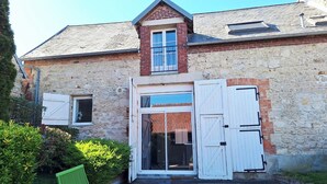 A stone building with a wooden door, a window, and a green chair outside. - La Grange de Marie studio 2 persons (Monampteuil)