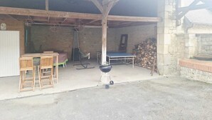 A covered outdoor area with a table, chairs, a hammock, a grill, and a stack of firewood. - La Grange de Marie studio 2 persons (Monampteuil)
