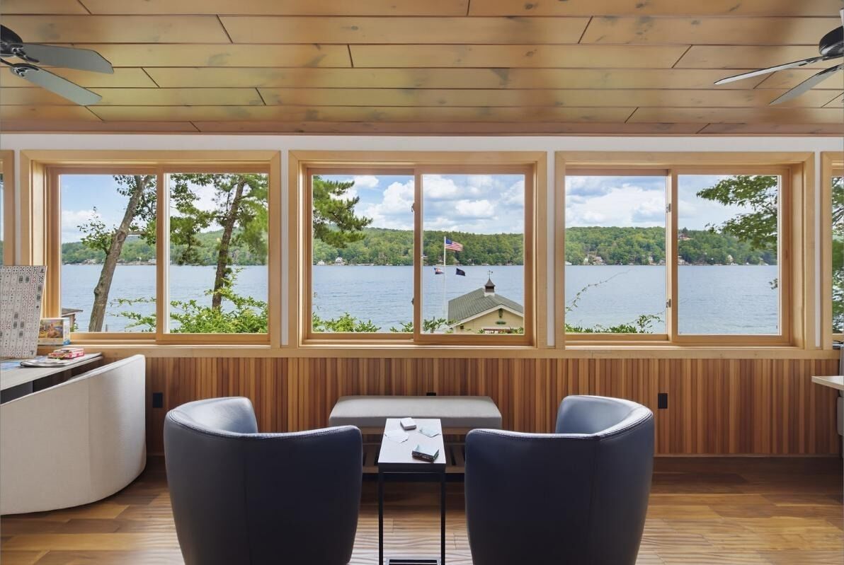 Una cabaña con interior de madera, amplias ventanas con vistas a un lago, zona de comedor y espacio de estar.