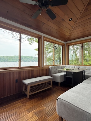 A cabin with a wooden interior, large windows, a ceiling fan, and a bench.