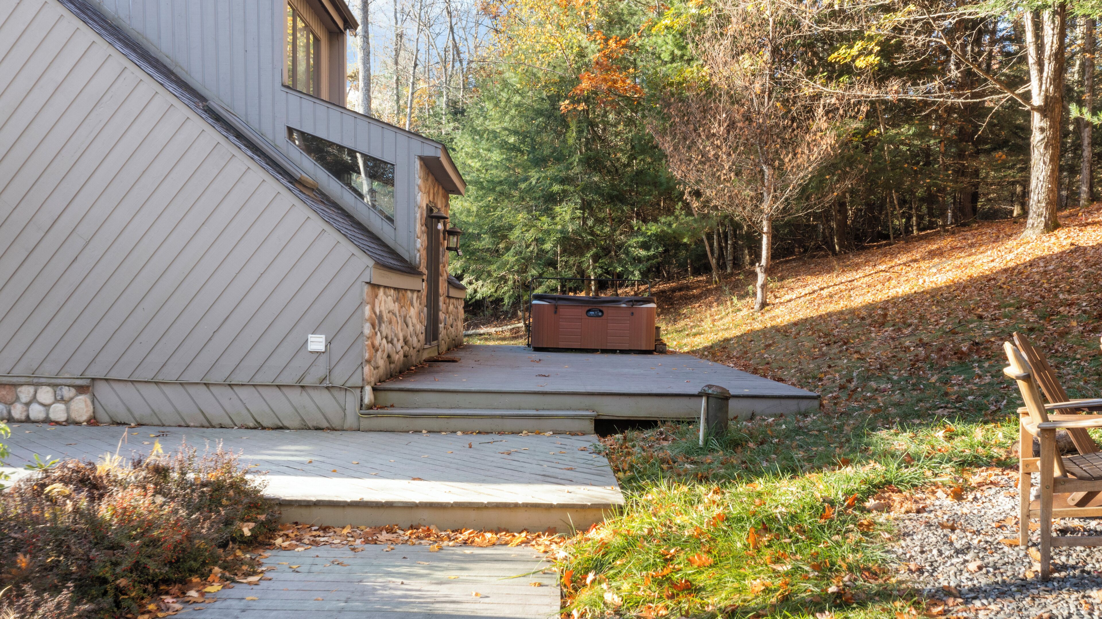 Une maison moderne avec des fondations en pierre, une terrasse en bois et un jacuzzi.