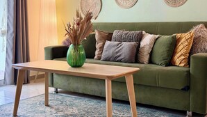 A green sofa with multiple cushions, a wooden coffee table, a green vase with dried plants, and wall decor. - Coastal 2BR Apt in Mackenzie Steps from Beach (Makenzy)