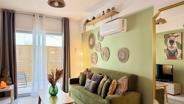 A living room with a green sofa, a coffee table, a TV, decorative wall art, and a large mirror. - Coastal 2BR Apt in Mackenzie Steps from Beach (Makenzy)