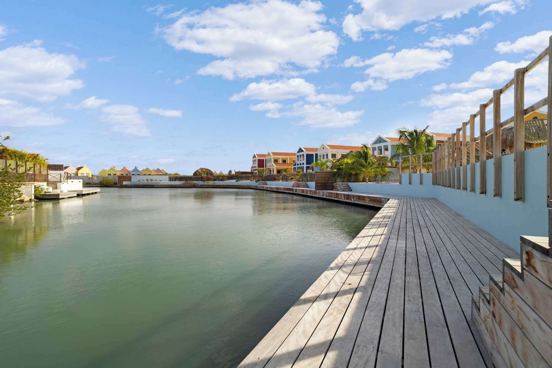 A waterfront property with a wooden deck, a calm water body, and colorful buildings in the background.