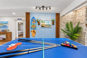 A pool table with pool cues and balls, a surfboard decoration, and a brick wall. - 6 King Suites | Pool + Game Room Oasis Near Beaches (Seminole)