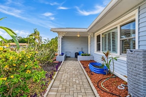 A house with a covered porch, a pathway leading to the entrance, and a garden with various plants and a blue water feature. - 6 King Suites | Pool + Game Room Oasis Near Beaches (Seminole)
