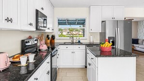 Een moderne keuken met witte kasten, een roestvrijstalen koelkast, een broodrooster en een raam met uitzicht op een woonwijk.