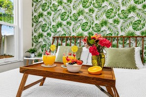 Una safata de fusta amb articles per esmorzar, un ram de flors i un fons de paper pintat amb motius tropicals.