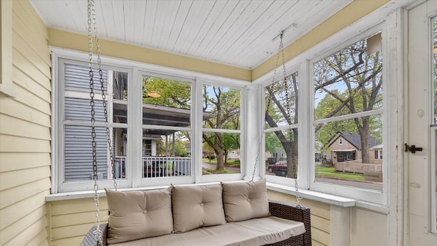 A wicker swing chair with cushions, a white ceiling, and large windows with a view of a residential area.