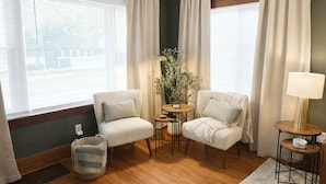 A room with two armchairs, a small table with a plant, a lamp, and a view through large windows.