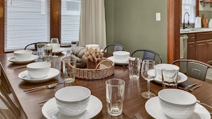 A dining area with a long wooden table set for four, equipped with white plates, glasses, and cutlery.