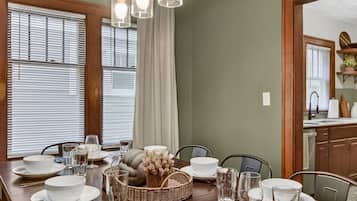 Un coin repas avec une longue table en bois, dressée pour quatre personnes, et agrémentée d’assiettes blanches, de verres et de couverts.