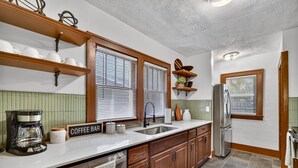A kitchen with wooden cabinets, a coffee bar sign, a refrigerator, and a sink.