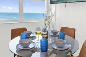 Een eettafel met kommen, glazen en een vaas met bloemen, voor een uitzicht op de oceaan.