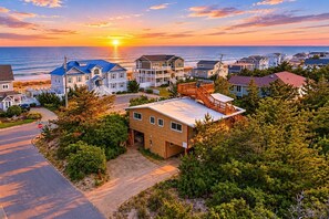 A coastal residential area with houses, a stop sign, and a clear view of the ocean at sunset.