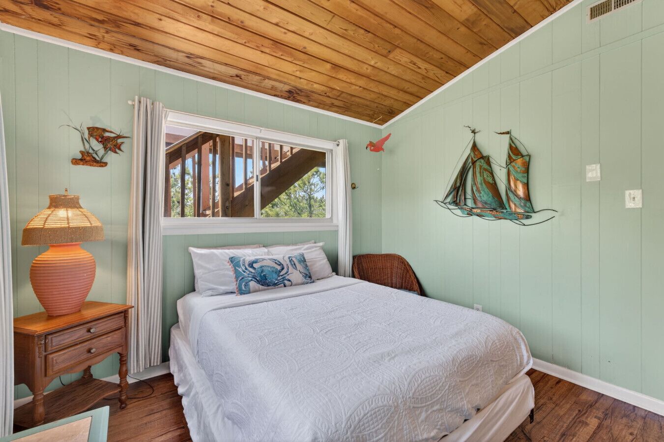 Un dormitorio con cama, mesita de noche, lámpara y ventana con vista a una terraza de madera.