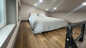 Un dormitori amb llit, terres de fusta, una finestra i una escala.