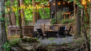 An outdoor seating area with a fire pit, surrounded by trees and a wooden deck.
