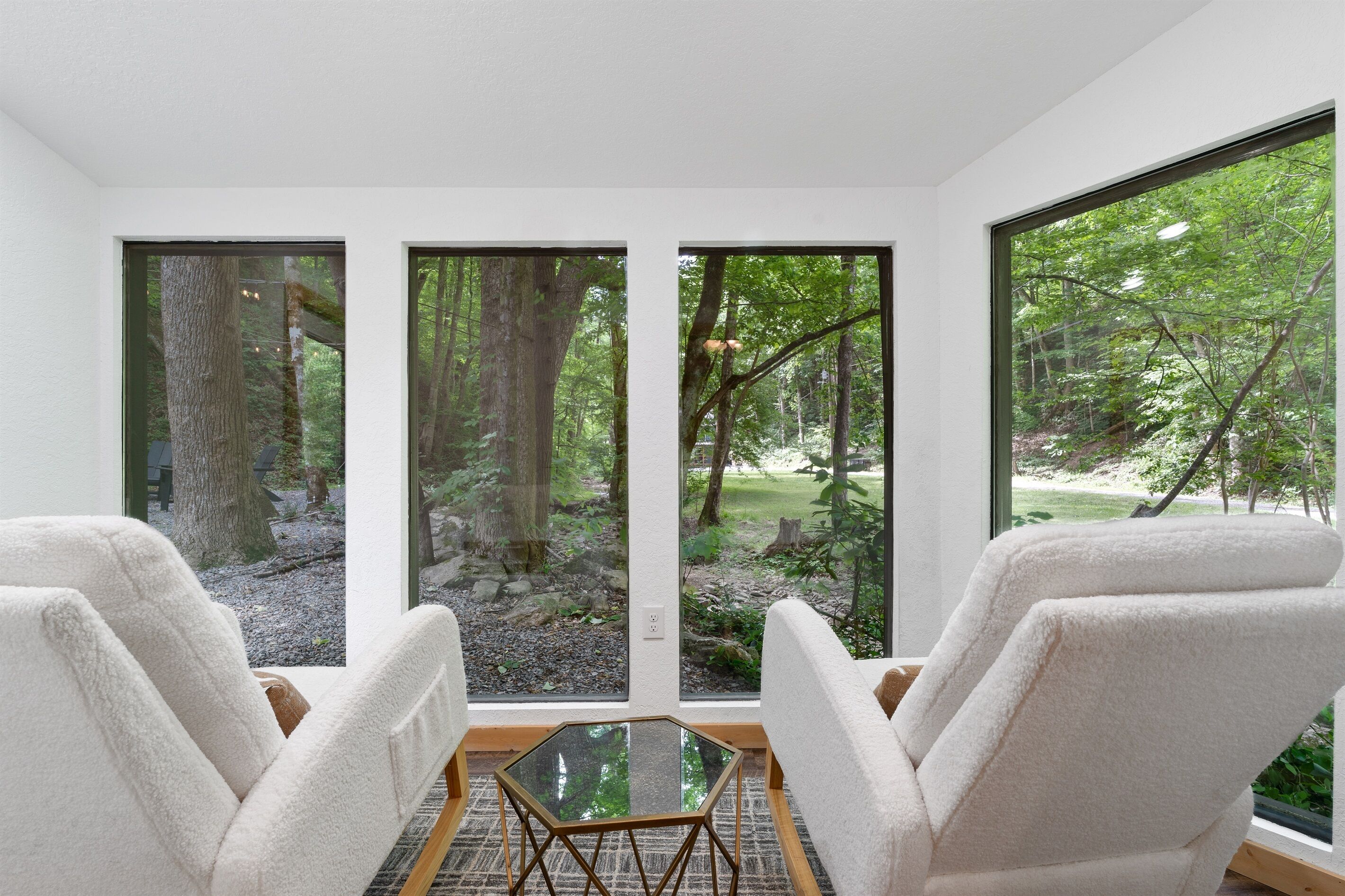 A room with three large windows, a glass table, and two white chairs.