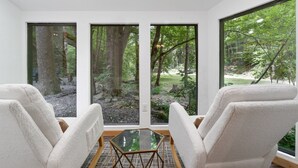 A room with three large windows, a glass table, and two white chairs.