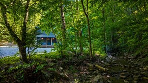 A cabin with a deck overlooking a forested area and a body of water.