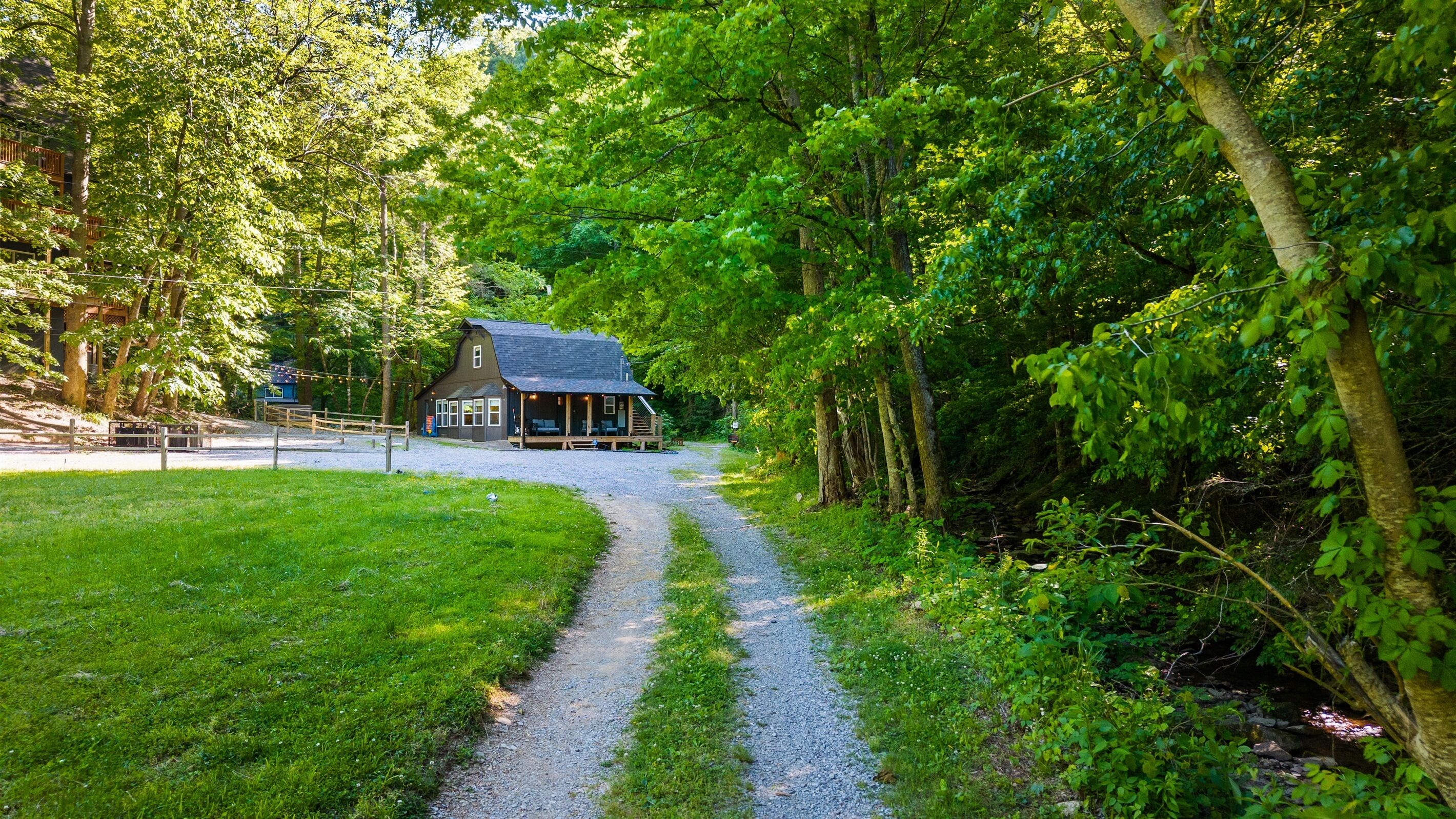 Un chalet rustique, accessible par un chemin de gravier, et entouré d’une végétation luxuriante.